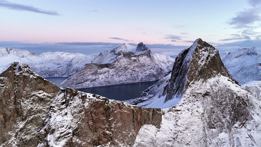 Cinematic aerial view of Segla peak on Senja Island, Norway, steep snow-covered cliffs above icy fjord, dramatic arctic landscape with rugged mountains and winter wilderness