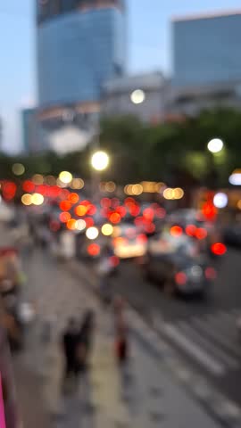 Blurred view of a busy city street at dusk, with traffic and streetlights creating a vibrant bokeh effect, capturing the energy of urban life and a rush hour commute.