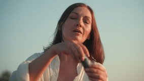 Close up of young woman blowing bubble wand to create translucent soap bubbles while smiling joyfully under clear sky, sunlight highlighting face as soft breeze carries bubbles across frame - Powered by Shutterstock - Get 15% off with code: PIKWIZARD15