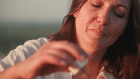 Close up of fair skinned woman blowing soapy bubble reflecting rainbow hues, gentle light illuminating lips and wand in soft focus outdoors, highlighting delicate bubble - Powered by Shutterstock - Get 15% off with code: PIKWIZARD15