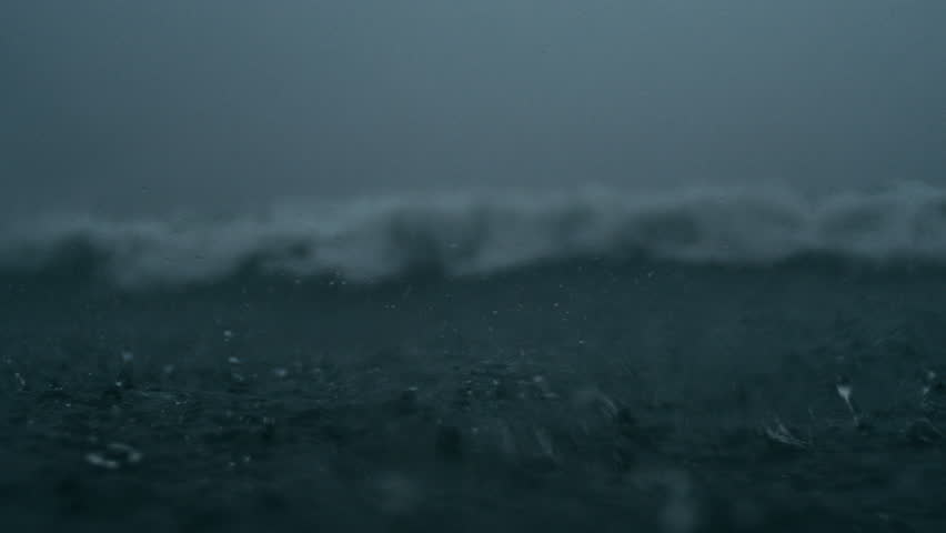 Dark ocean waves distort as raindrops fall in slow motion beneath storm skies