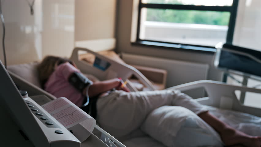 Close-up of a fetal monitor in a doctor's office, displaying fetal heart rate and uterine contraction data during a prenatal check-up with a blurred view of a pregnant woman lying in a hospital bed - Powered by Shutterstock - Get 15% off with code: PIKWIZARD15