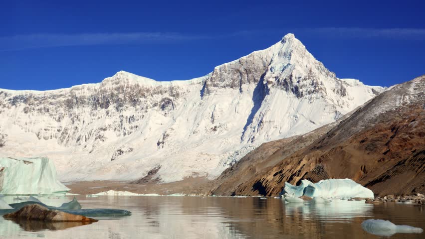 Static video shot of Mount San Lorenzo covered in snow, with icebergs floating on calm waters under a clear blue sky in Perito Moreno National Park ,Patagonia, Argentina.