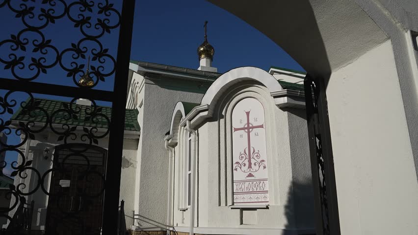 Modern Orthodox church with white walls, green roof and golden domes with crosses during the day