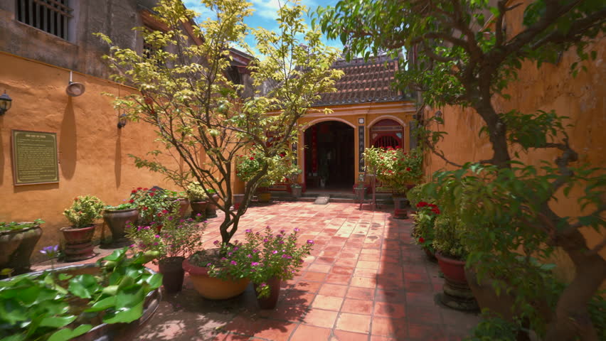 Courtyard establishing of temple with ochre walls, lanterns, and greenery in Hoi An, Vietnam, smooth establishing dolly