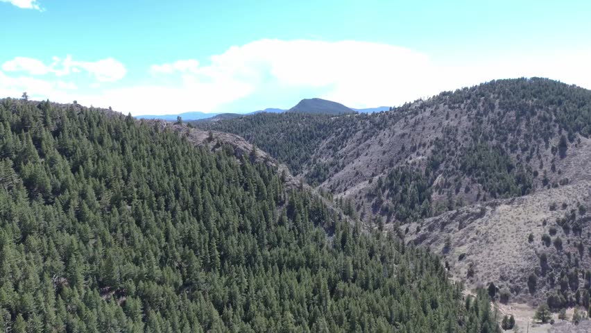Aerial view of Colorado Rockies valleys with a winding mountain drive. Sunlight breaks through clouds, highlighting peaks and forests. Ideal for travel, adventure, or nature visuals.