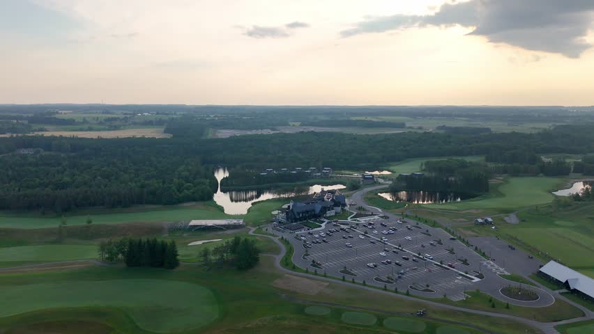 Drone orbit over golf course with trimmed fairways, water traps reflect sky, large open parking lot