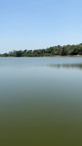 Close-up view of fresh vibrant beauty of ambika river water flow, hill, trees, grass, sunlight and blurry greenery nature with blue cloudy sky environment in the outdoor indian village tourist place.