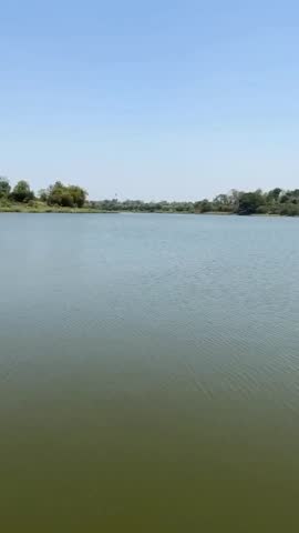 Close-up view of beautiful fresh vibrant ambika river water flow, hill, trees, grass, sunlight and blurry greenery nature with blue cloudy sky environment in the outdoor indian village tourist place.