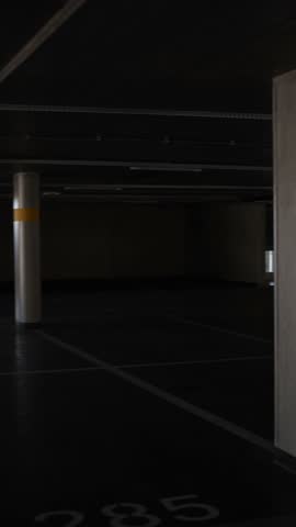Vertical screen empty underground parking garage with concrete pillars dim artificial light and daylight streaming through side windows creating urban atmosphere of silence and modern architecture