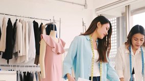 Two young fashion designers collaborate in bright studio. Tailoring teamwork at boutique startup with fabric, patterns, garments, mannequins, and rack. Seamstress entrepreneur spirit shown. - Powered by Shutterstock - Get 15% off with code: PIKWIZARD15