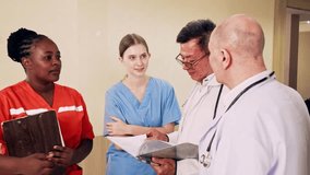 Diverse medical team of doctors and nurses meet in hospital corridor. Wearing scrubs and coats, they hold a discussion with clipboard, showing healthcare teamwork, collaboration, and patient care. - Powered by Shutterstock - Get 15% off with code: PIKWIZARD15