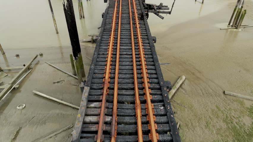 Blackened Railway Tracks Stretch Across the Muddy Riverbed in Richmond, British Columbia, Canada - Aerial Pullback Shot