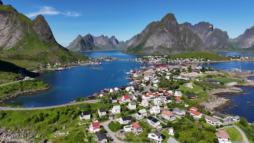 Aerial footage of the fishing village Reine, nestled between steep mountains and surrounded by mirror-like reflective waters in the Lofoten Islands, Norway.