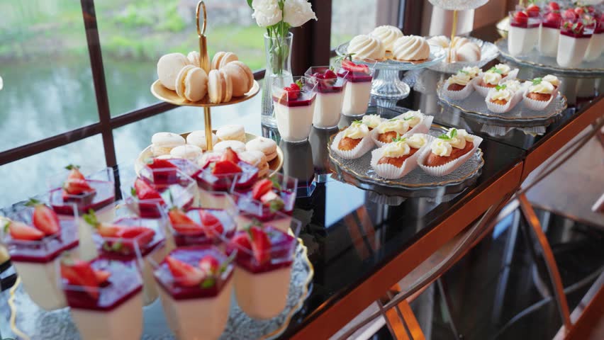 Elegant dessert table with a variety of gourmet sweets including panna cotta, macarons, mini cakes, and fruit desserts beautifully arranged for a wedding or upscale celebration.