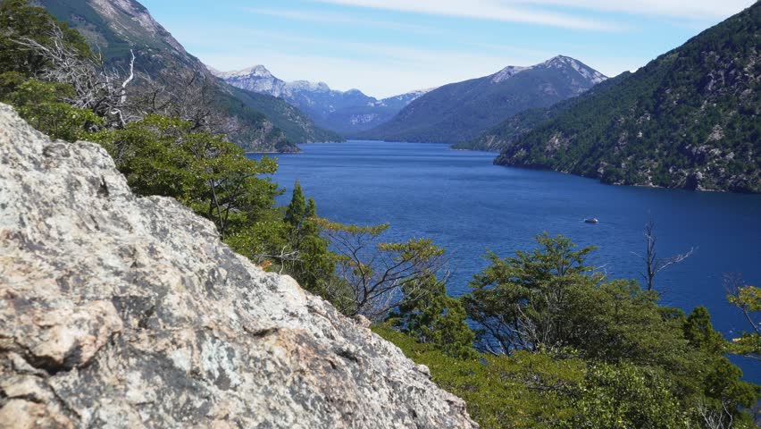 Static shot from Bahía López viewpoint overlooking Brazo de la Tristeza with lenga forests and a ship passing by. Nahuel Huapi National Park, Bariloche, Patagonia, Argentina.