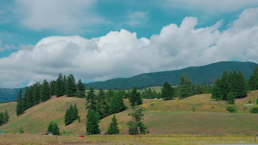 A time-lapse of a cloudy sky over a hilly landscape with sparse trees and mountains