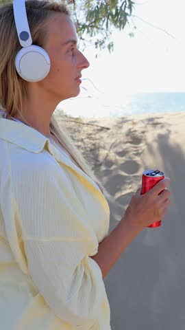Woman Drinking from Red Can with Headphones Outdoors