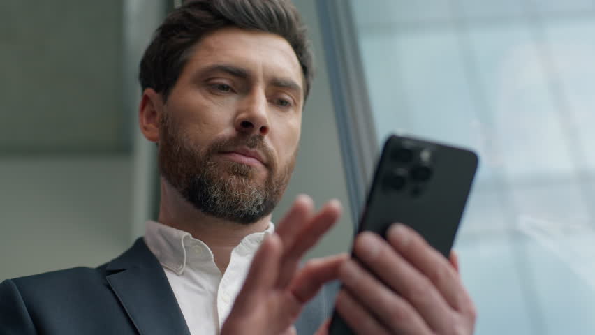 Calm Caucasian 40s businessman using mobile phone in office looking out window male specialist entrepreneur pensive business man chatting smartphone online e-commerce modern technology checking emails - Powered by Shutterstock - Get 15% off with code: PIKWIZARD15