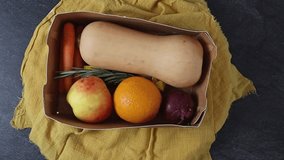 One cardboard box with fresh pumpkin, carrot, apple, orange, onion, garlic, bouillon cubes and rosemary sprigs on black stone background with yellow kitchen cloth,flat lay close-up with zoom out. Holi - Powered by Shutterstock - Get 15% off with code: PIKWIZARD15