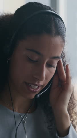 Vertical shot of young elegant female operator with headset speaking in microphone and taking notes in notepad while sitting by desk and consulting clients of marketplace
