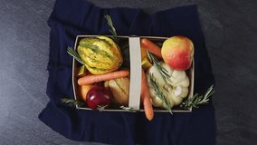 Unrecognizable young Caucasian girl picks up wooden box with pumpkin, carrot, apple, orange, onion, garlic, bouillon cubes and rosemary sprigs on black stone background, close-up in slow motion in rea - Powered by Shutterstock - Get 15% off with code: PIKWIZARD15