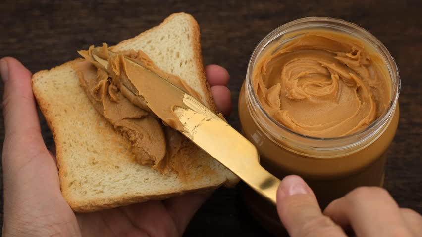 Spreading peanut butter on a piece of toast bread. Making breakfast toast