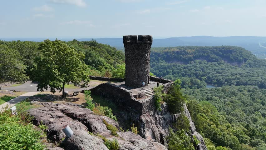 Drone view of Castle Craig atop East Peak in Hubbard Park, Meriden, CT. Historic stone tower surrounded by forest, scenic hills, and panoramic New England landscape.