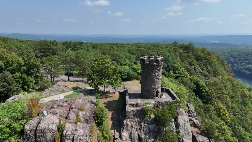 Drone view of Castle Craig atop East Peak in Hubbard Park, Meriden, CT. Historic stone tower surrounded by forest, scenic hills, and panoramic New England landscape.