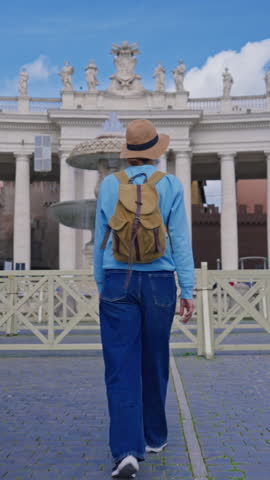  A girl tourist in a hat and with a backpack walks along as she admires the iconic St. Peters Square in Vatican City, Italy, 29.04.2025