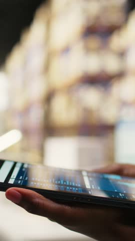 Vertical Video Close up of distribution hub worker overseeing supply chain process for e-commerce. Reviewing logistics and shipping data on tablet, updating tracking labels for order fulfillment