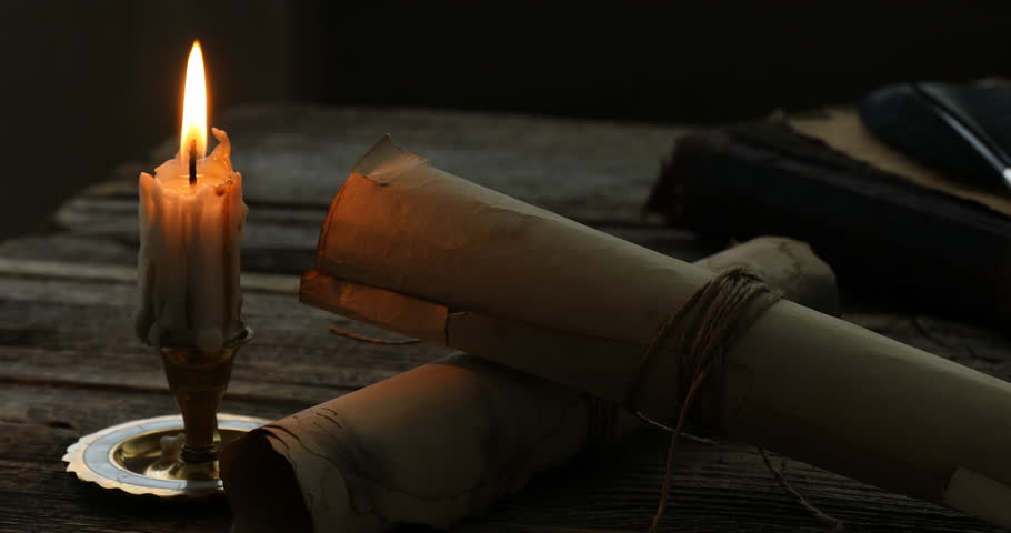 Old rolled scrolls and burning candle on wooden table, closeup