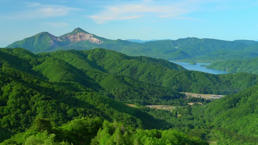 Green mountain landscape with forest, hills, and a lake on a sunny day