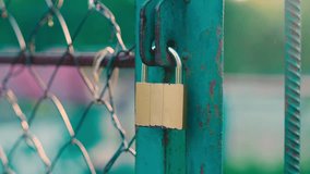 Close-Up Detail Shot: Brass Padlock on Turquoise Metal Sports Court Gate | Chain Link Fence Security with Warm Sunset Lighting | Urban Recreation Area Access Control - Powered by Shutterstock - Get 15% off with code: PIKWIZARD15