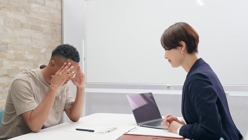 A Japanese female staff member interviewing a troubled black man