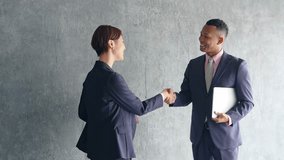 A black male businessman and a Japanese female staff member shaking hands in a stylish room - Powered by Shutterstock - Get 15% off with code: PIKWIZARD15