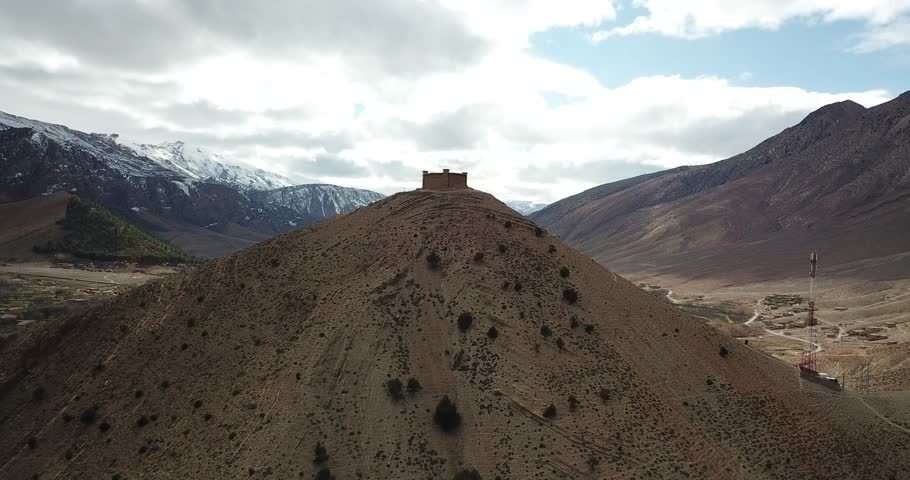 An ancient kasbah crowns a hilltop in Morocco's Atlas Mountains, its red clay walls and defensive towers standing proud against dramatic peaks and endless mountain vistas