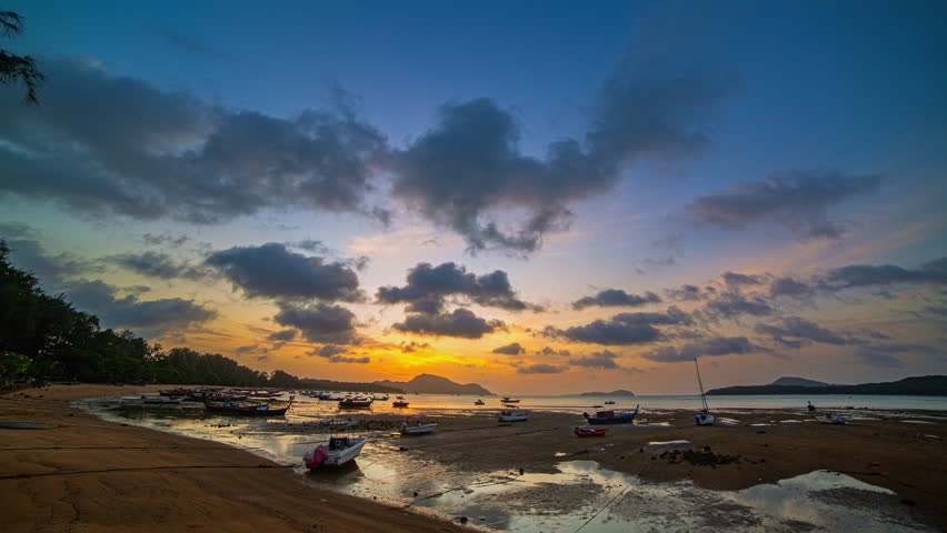 Time lapse Tranquil Sunrise.
A vivid tropical sunrise paints the sky with brilliant hues of orange, pink, and gold as gentle waves lap the shore. Traditional boats float peacefully on the calm sea