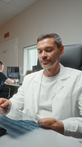 Medic expert holding x ray imaging test results. Handsome Caucasian male reviewing diagnostic results. Concentrating inside radiology room. Neuroscientist Finding Treatment X-ray Scan MRI CT Scan
