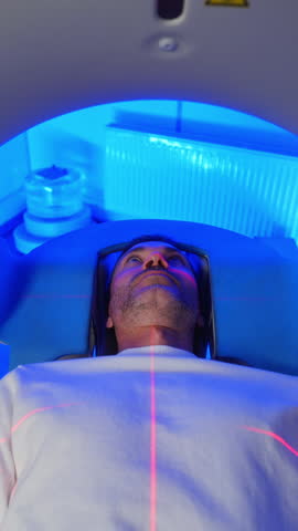 Portrait Shot of a male Patient Lying on a CT or MRI Scan, Bed is Moving Inside the Machine While it Scans Body and Brain. In Medical Laboratory with High-Tech Equipment. Top Down View