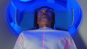 Medical Laboratory or Healthcare Facility with High-Tech Equipment: Portrait Shot of Male Patient Lying on a CT or MRI Scan, Bed is Moving Inside the Machine While it Scans Brain. Top Down View - Powered by Shutterstock - Get 15% off with code: PIKWIZARD15