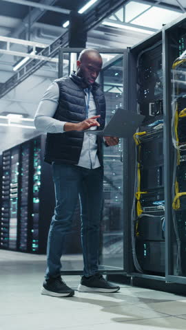 Vertical Screen: African Programmer Using Laptop Computer, Focused while Inputting Data. Cloud Computing Server Farm System Administrator Working on IT Maintenance for Saas Business Company