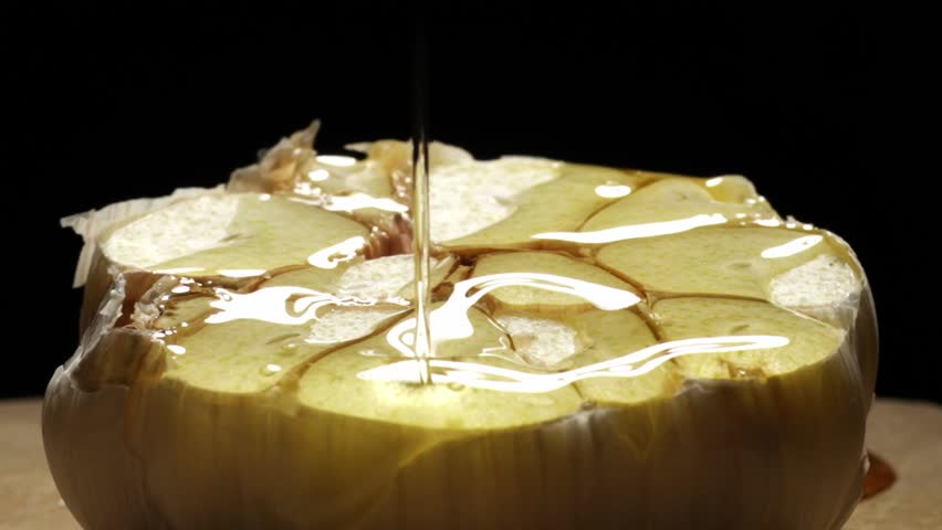Close up pouring oil over a garlic cloves. Black background