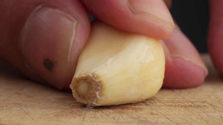 Person cutting garlic in wooden board. Macro close-up