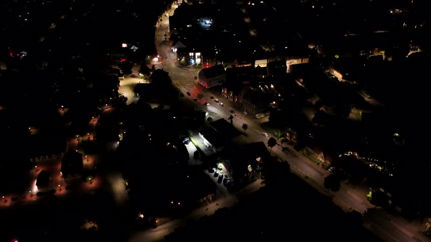 Driving cars on main street of small town at night. American housing area with warm lighting streetlights. Aerial wide shot. Row of houses in historic city. Junction with glowing lanterns in summer.