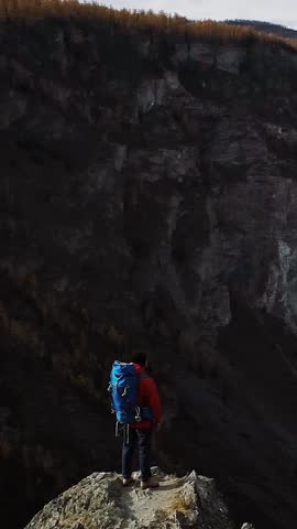 Backpacker with raised arms celebrating reaching mountain peak, enjoying inspiring view of valley and snow-capped peaks of Altai Mountains in autumn