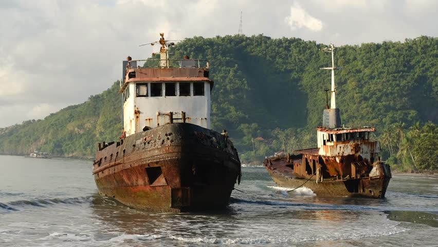 Two abandoned rusty ships near the shore at sunrise with mountains in background