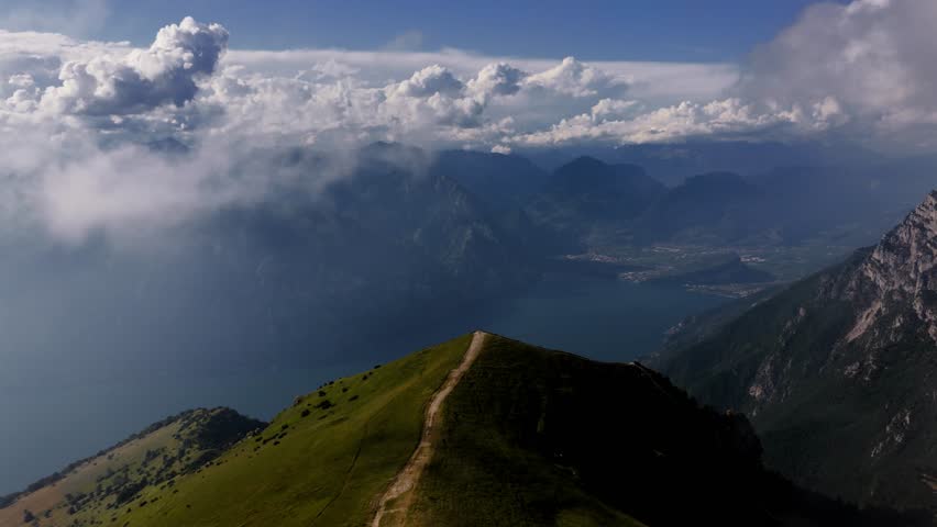 Aerial orbit flight through clouds over Monte Baldo with panoramic view of Lake Garda and dramatic mountain ridges in the Italian Alps