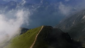 An aerial orbit shot moving from right to left with a smooth pullback, revealing a mountain ridge covered in green slopes and surrounded by drifting clouds, with layers of dramatic peaks fading into - Powered by Shutterstock - Get 15% off with code: PIKWIZARD15