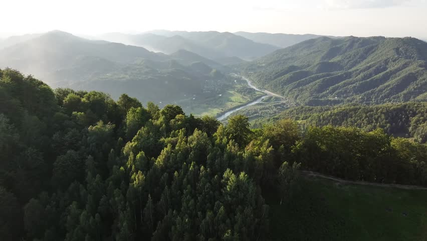 Flight over the summer mountains with mountain river serpentine, green meadows, village and forest. Ukraine, Carpathians